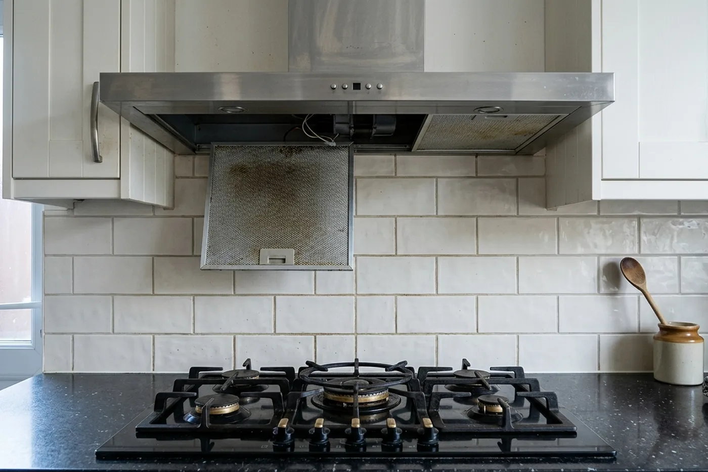 A five burner gas hob with cast iron pan supports beneath a stainless steel extractor hood
